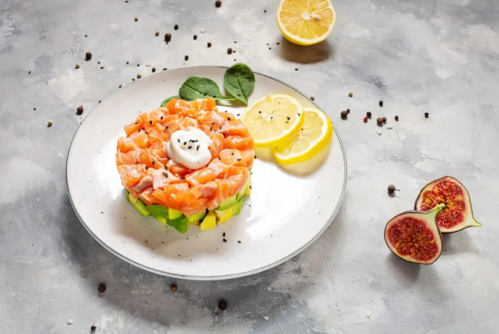 Avocado and salted salmon tartar topped with fresh lemon slices and figs on a white plate