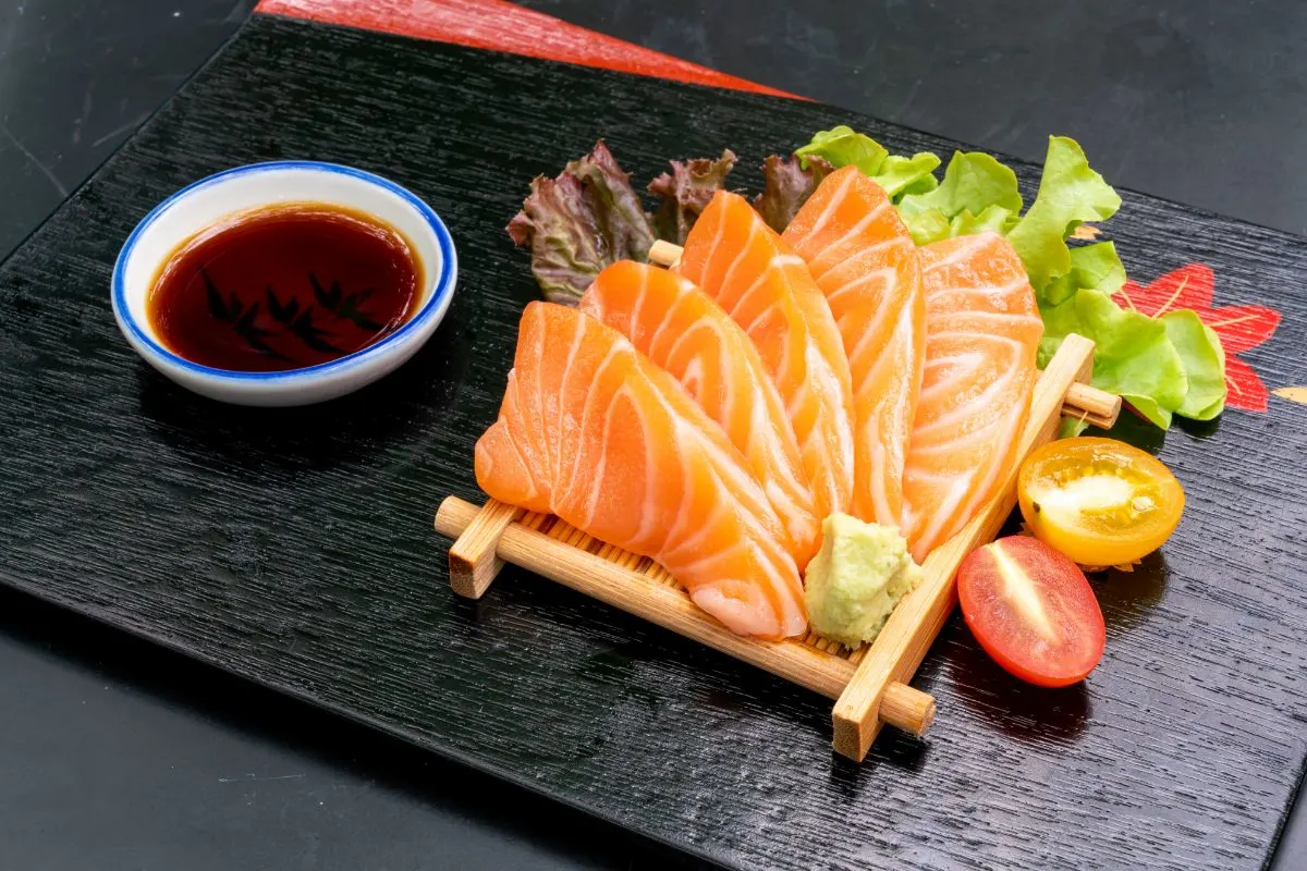 Fresh raw salmon sashimi served with a side of soy sauce, garnished with wasabi and ginger