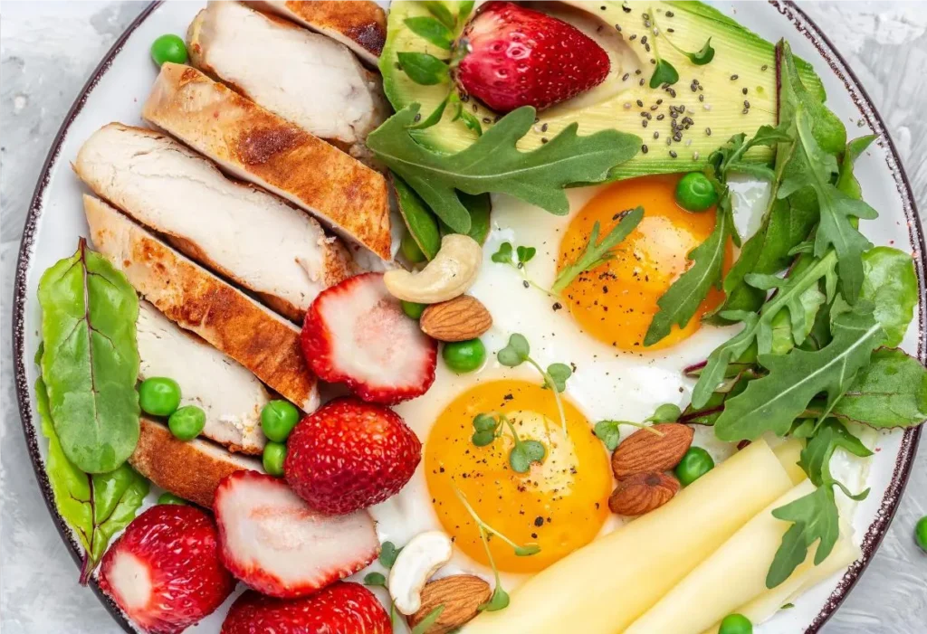 Easy High Protein Breakfast - Healthy protein breakfast plate with grilled chicken, fried eggs, avocado, strawberries, arugula, almonds, cheese, and peas.