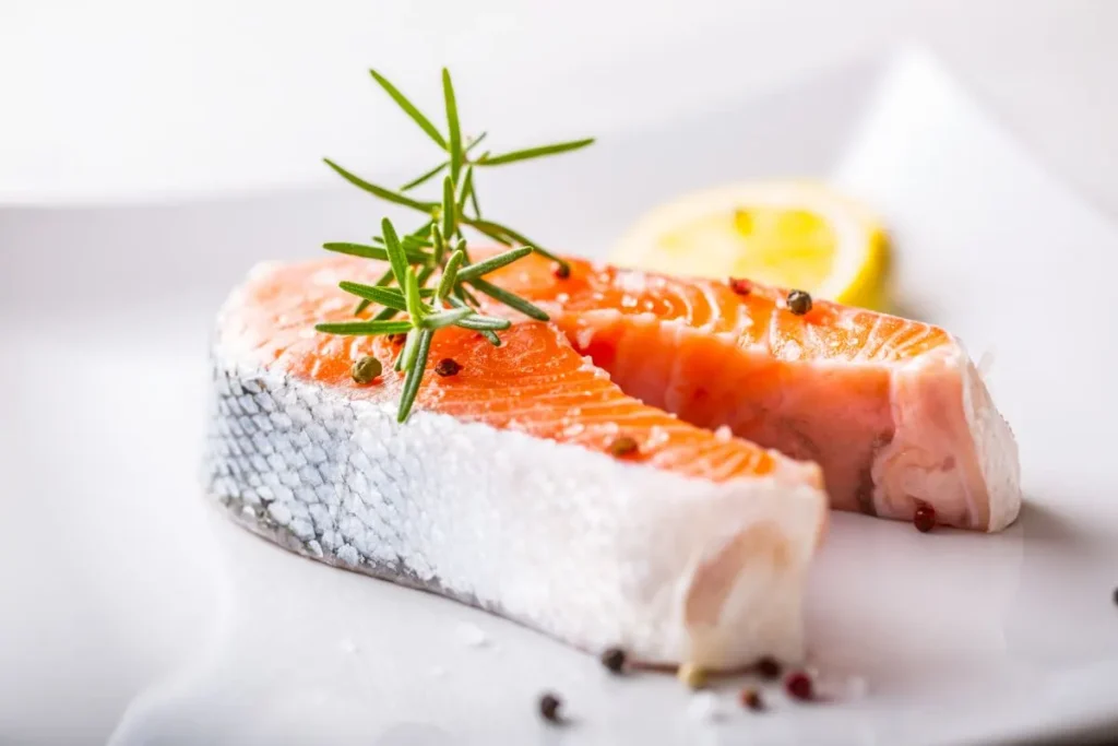 Is King Salmon Better Than Regular Salmon? Raw salmon steak with rosemary, lemon, salt, and pepper on a wooden board