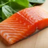 Close-up of flaky fish and glossy greens highlighting salmon spinach recipe.
